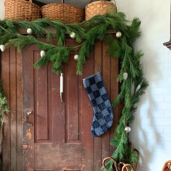 fresh white pine garland lining a dark vintage wooden cabinet and a checkered blue stocking for a gorgeous vintage christmas display