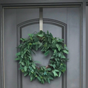 a green wreath hung on a door with a metal wreath hook