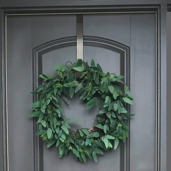 a green wreath hung on a door with a metal wreath hook